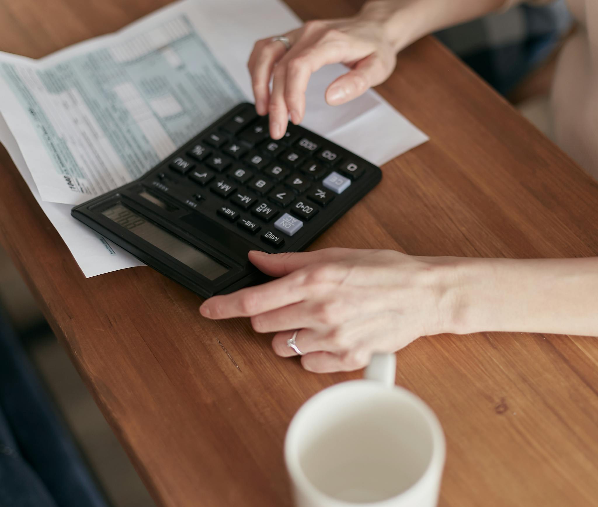 About A woman uses a calculator to manage finances at home, focused on budget planning.