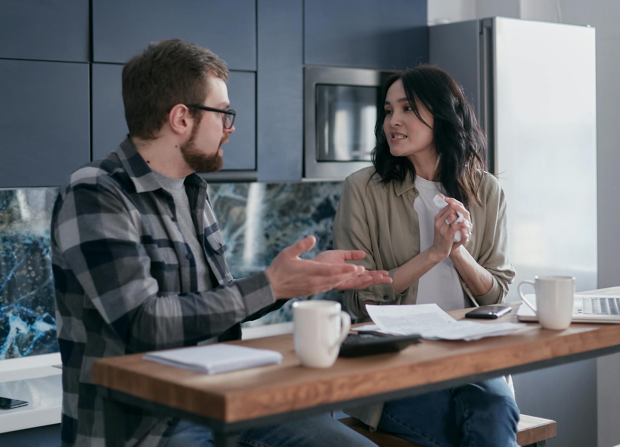 A young couple having a serious discussion about finances in their kitchen.
